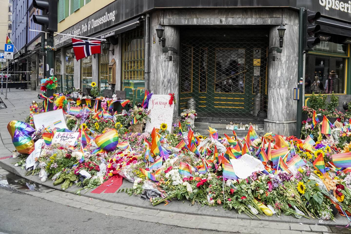 Bildet viser blomster og regnbueflagg utenfor utestedene som ble angrepet natt til 25. juni. Politiet etterforsker om hatkriminalitet var motiv for skytingen.