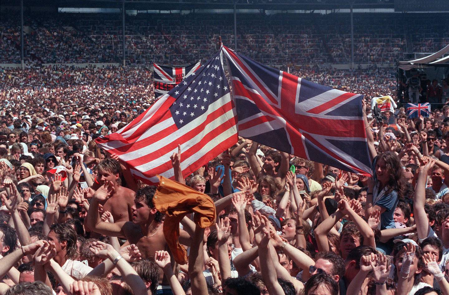 Fans wave flags, the U.S. Stars and Stripes and Britain's Union Jack, at Wembley Stadium, London, July 13, 1985, at the end of the Live Aid famine relief concert for Africa. (AP Photo/Joe Schaber)