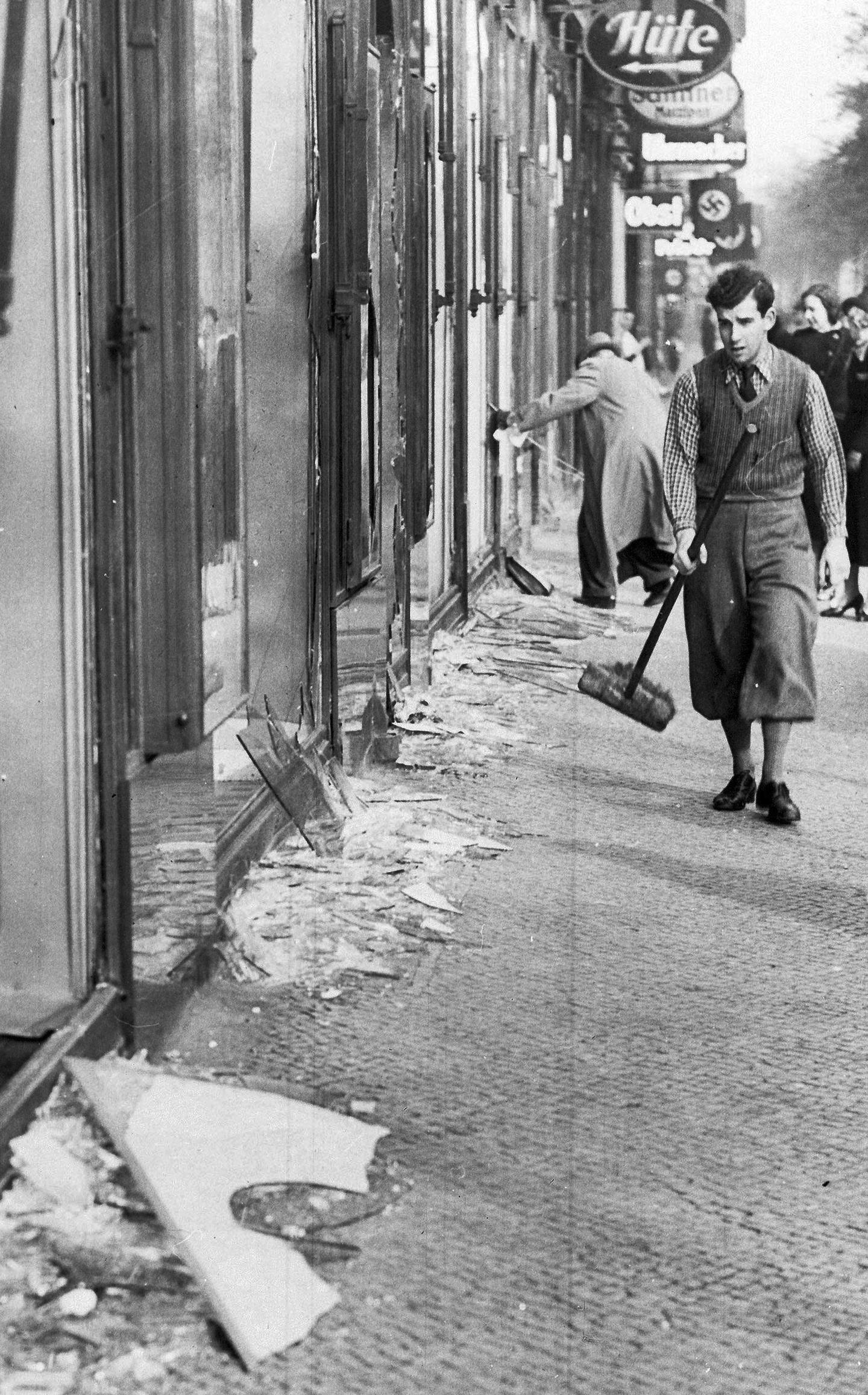 RYDDER OPP: 10. november 1938 går en ung mann med en kost ut på gaten for å rydde opp det knuste glasset utenfor en  jødisk butikk i Berlin, dagen etter Krystallnatten.