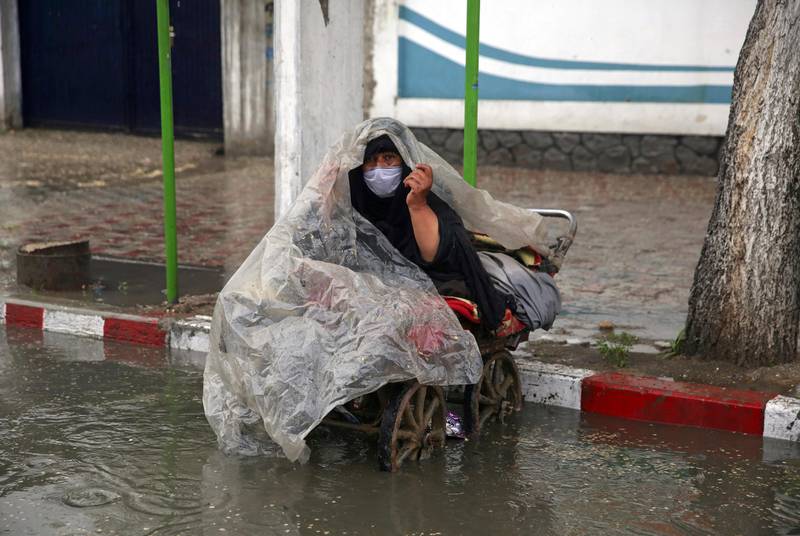 A woman waits to receive alms as she covers herself with a plastic sheet in the rain and wears a protective face mask to help curb the spread of the coronavirus during a quarantine in the holy fasting month of Ramadan in Kabul, Afghanistan, Tuesday, April 28, 2020. Muslims across the world are observing Ramadan when the faithful refrain from eating, drinking and smoking from dawn to dusk. (AP Photo/Rahmat Gul)