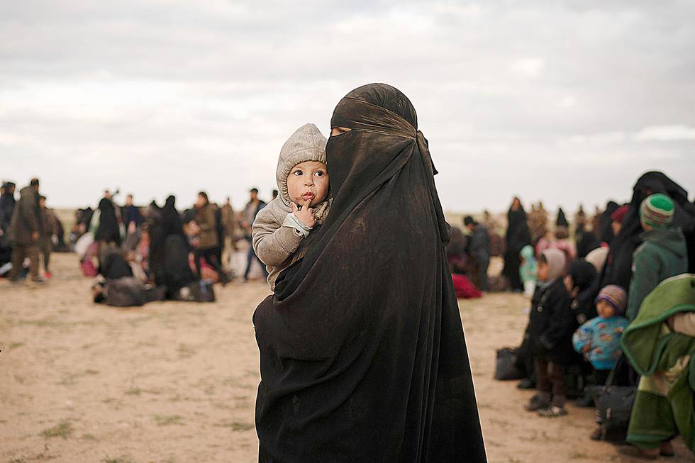 A woman holds a child as she waits to be screened by U.S.-backed Syrian Democratic Forces (SDF) after being evacuated out of the last territory held by Islamic State militants, in the desert outside Baghouz, Syria, Wednesday, Feb. 27, 2019. (AP Photo/Felipe Dana)