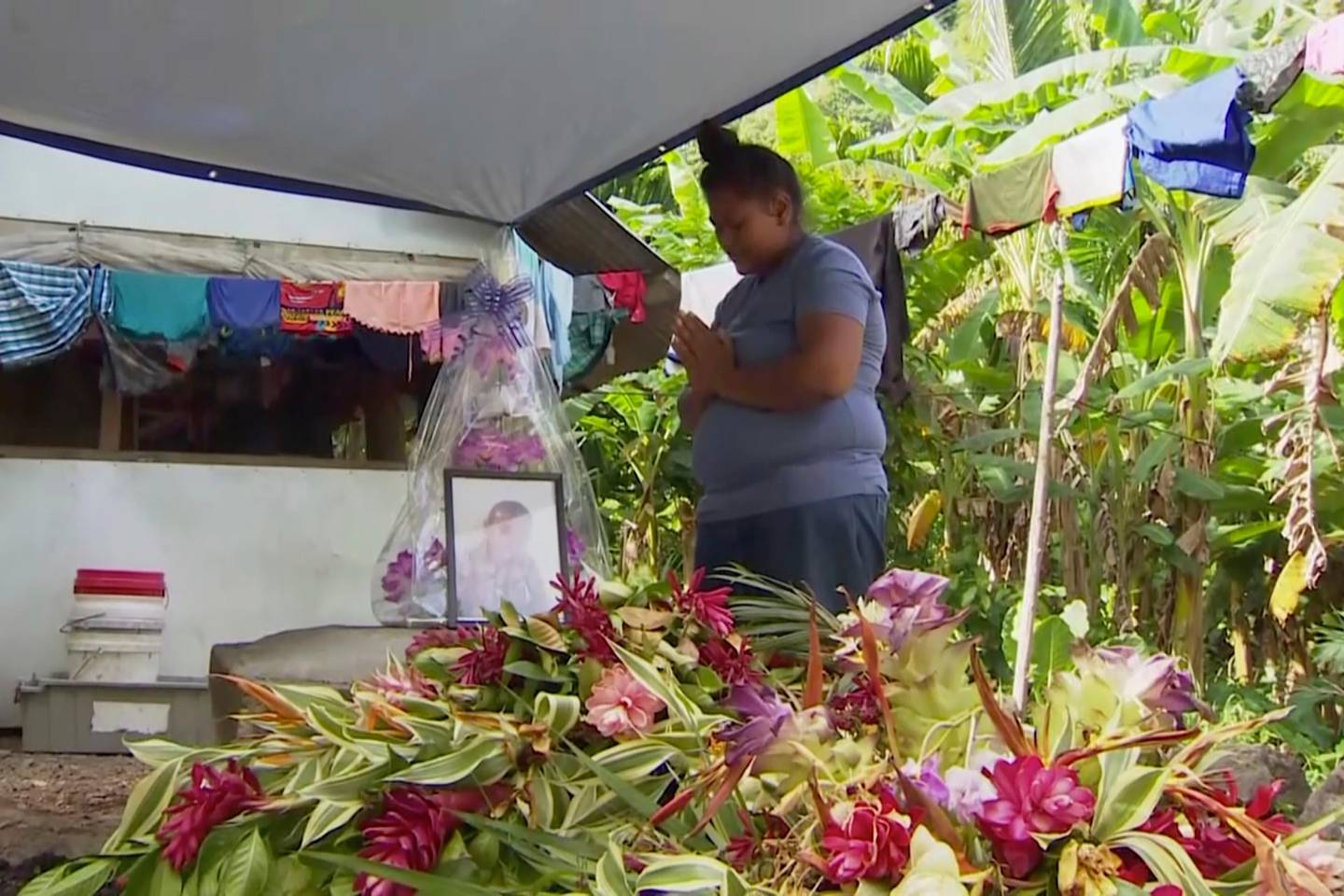 In this November 2019, image from video, a woman prays in front of a portrait of her lost child with measles in Apia, Samoa. Samoa closed all its schools on Monday, Nov. 18, 2019, banned children from public gatherings and mandated that everybody get vaccinated after declaring an emergency due to a measles outbreak. For the past three weeks, the Pacific island nation of 200,000 people has been in the grip of a measles epidemic that has been exacerbated by low immunization rates. (TVNZ via AP)