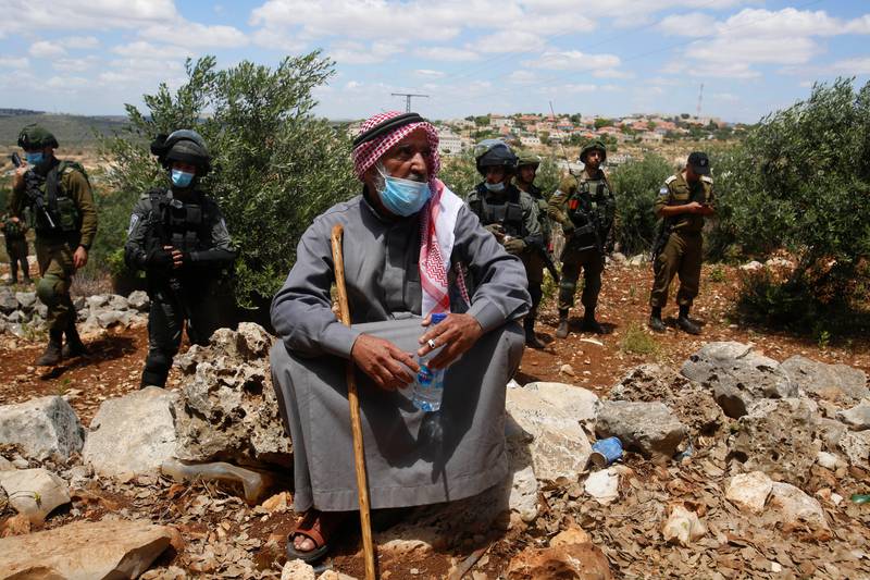 A Palestinian man sits in front of Israeli troops during a protest against Israeli settlements, near the West Bank city of Salfit, Friday, May 29, 2020. (AP Photo/Majdi Mohammed)