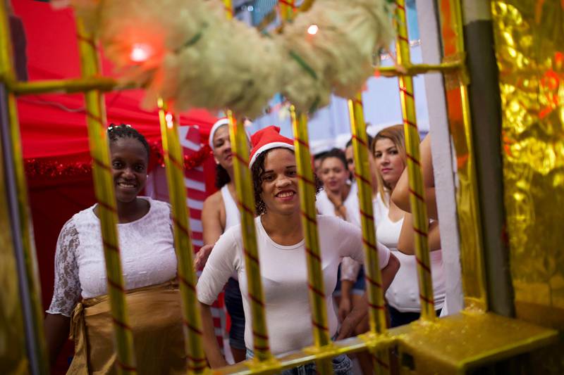 Inmates smile behind prison bars covered in decorative paper, part of a Christmas decoration contest at the Nelson Hungria Prison in Rio de Janeiro, Brazil, Thursday, Dec. 13, 2018. Inmates serving time for offenses from burglary to homicide spent weeks decking out their cell blocks with handmade Christmas decorations and planning Bible related performances for the jail's annual Christmas event. (AP Photo/Silvia Izquierdo)