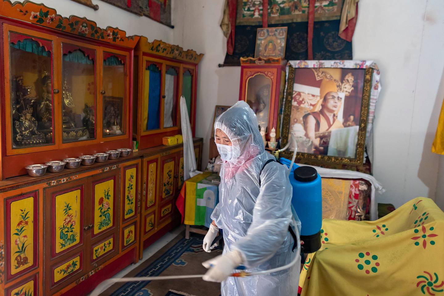 A portrait of the Tibetan spiritual leader the Dalai Lama adorns a prayer room as an employee of the Central Tibetan Administration in protective clothing sprays a steriliser as a precaution against the coronavirus in Dharmsala, India, Thursday, March 19, 2020. For most people, the new coronavirus causes only mild or moderate symptoms. For some it can cause more severe illness. (AP Photo/Ashwini Bhatia)