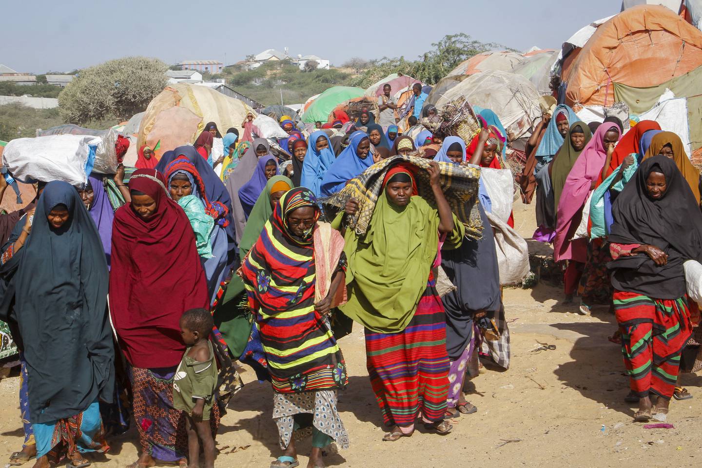 Somalis who fled drought-stricken areas carry their belongings as they arrive at a makeshift camp on the outskirts of the capital Mogadishu, Somalia Friday, Feb. 4, 2022. Thousands of desperate families have fled a severe drought across large parts of Somalia, seeking food and water in camps for displaced people outside the capital. (AP Photo/Farah Abdi Warsameh)
