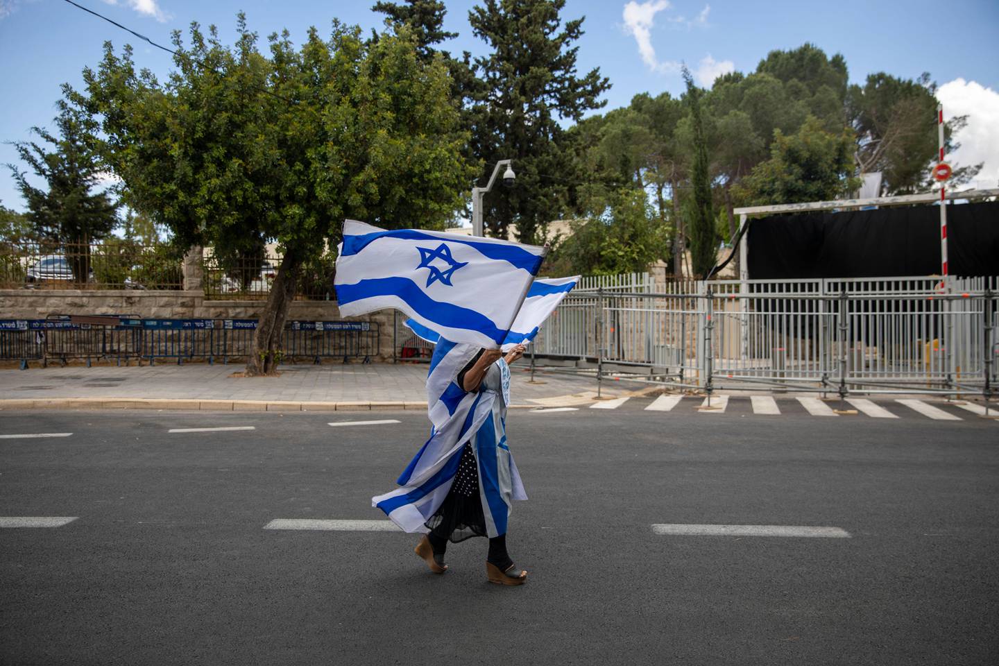 A supporter of Israel's Prime Minister Benjamin Netanyahu waves flags outside his residence in Jerusalem, Sunday, May 24, 2020. Hundreds of protesters calling him the "crime minister" demonstrated outside his official residence, while hundreds of supporters, including leading members of his Likud party, rallied in support of him at the courthouse. Netanyahu faces charges of fraud, breach of trust, and accepting bribes in a series of corruption cases. (AP Photo/Ariel Schalit)
