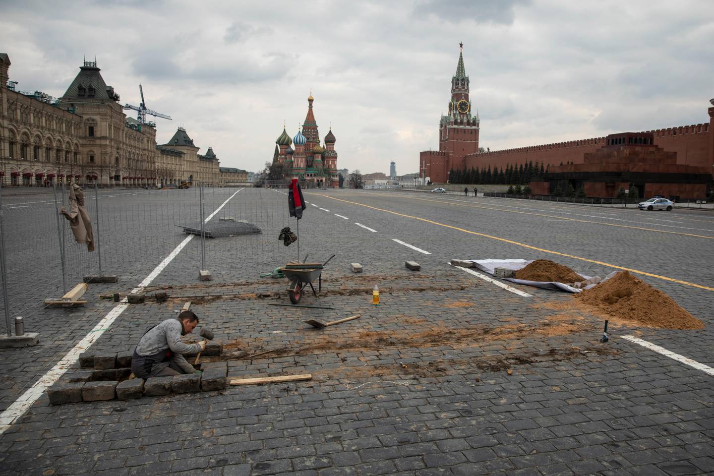 A worker fixes paving stones in emptied Red Square, with St. Basil's Cathedral, center, and Kremlin's Spasskaya Tower, right, in the background, in Moscow, Russia, Wednesday, April 8, 2020. The Russian capital has woken up to a lockdown obliging most people in the city of 13 million to stay home. The government ordered other regions of the vast country to quickly prepare for the same as Moscow, to stem the spread of the new coronavirus. The new coronavirus causes mild or moderate symptoms for most people, but for some, especially older adults and people with existing health problems, it can cause more severe illness or death. (AP Photo/Pavel Golovkin)
