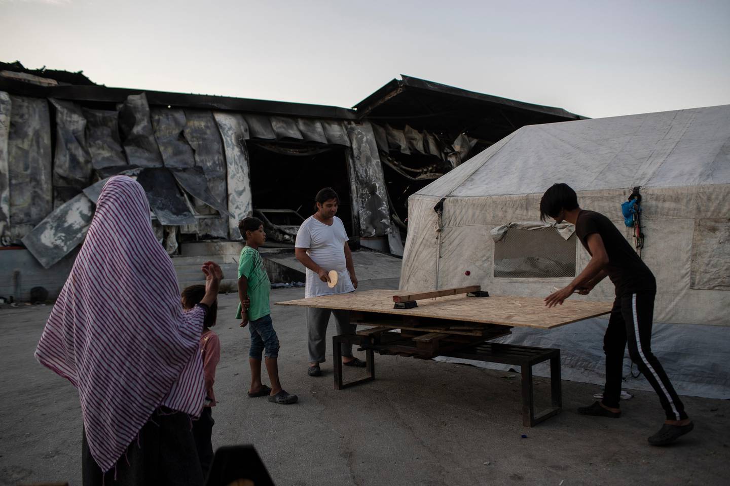 Migrants play table tennis on a makeshift table at the burned Moria refugee camp, on the northeastern island of Lesbos, Greece, Monday, Sept. 14, 2020. Greece's prime minister demanded Sunday that the European Union take a greater responsibility for managing migration into the bloc, as Greek authorities promised that 12,000 migrants and asylum-seekers left homeless after fire gutted an overcrowded camp would be moved shortly to a new tent city. (AP Photo/Petros Giannakouris)