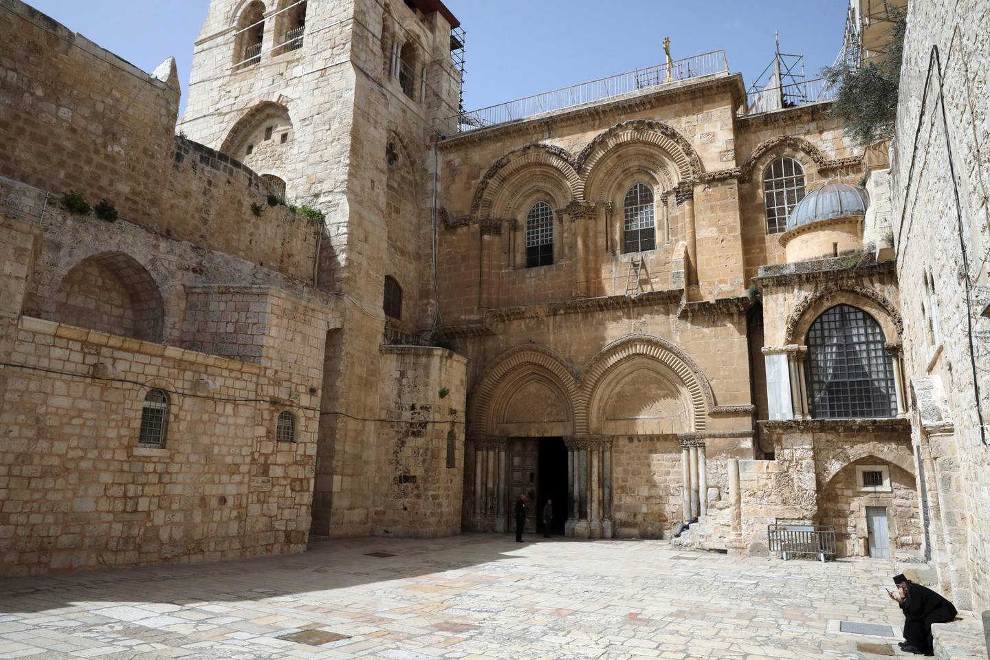 An Orthodox Christian priest checks his phone at an empty plaza in front to the Church of the Holy Sepluchre, where Christians believe Jesus Christ was buried, in Jerusalem, Monday, March 23, 2020. In Israel daily life has largely shut down with coronavirus cases multiplying greatly over the past week, (AP Photo/Mahmoud Illean)