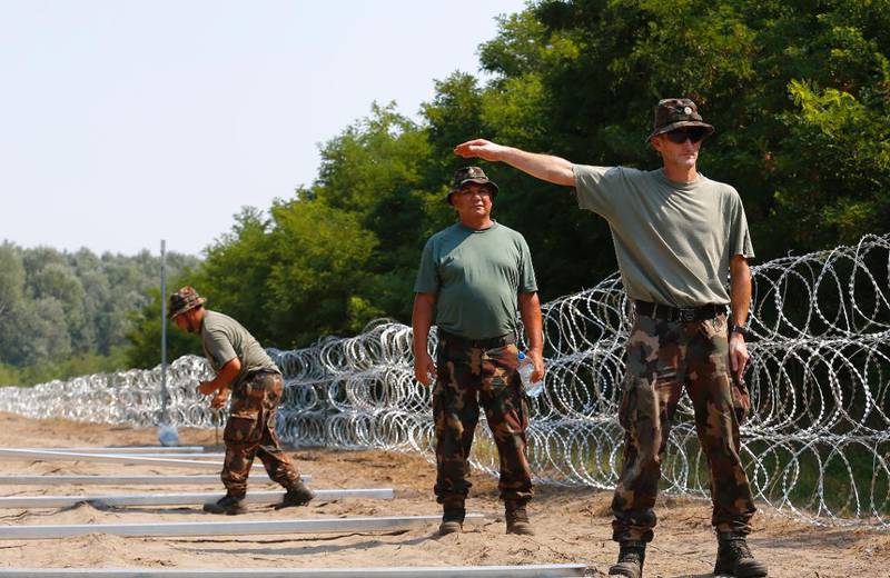 Ungarske soldatar har i heile sommar bygt eit fire meter høgt piggtrågjerde langs den 175 kilometer lange grensa mot Serbia. Her reiser tre soldatar gjerdepålar ved grenselandsbyen Asotthalom.