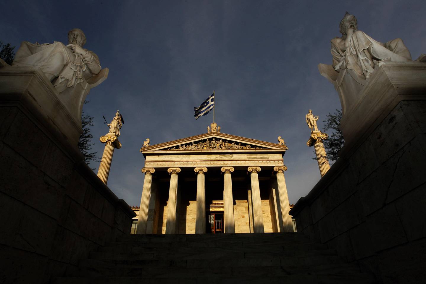 In this photo taken Friday, Oct. 21, 2011, marble statues of ancient Greek philosophers Socrates, right, and Plato, left, are seen on plinths in front of the Athens Academy, as the Greek flag flies. More than 200 international philosophers braved strikes and protests to come to Greece this month to join a forum and debate matters of the mind. Greece's illustrious ancient thinkers built the foundations of Western scholarship, and their philosophy stands as an unquantifiable source of national wealth even during a financial crisis. (AP Photo/Petros Giannakouris)