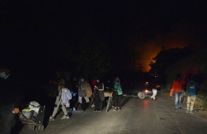 Refugees and migrants leave as fire burns at the Moria refugee camp on the northeastern Aegean island of Lesbos, Greece, on Wednesday, Sept. 9, 2020. Fire Service officials say a large refugee camp on the Greek island of Lesbos has been partially evacuated despite a COVID-19 lockdown after fires broke out at multiple points around the site early Wednesday. (AP Photo/Panagiotis Balaskas)