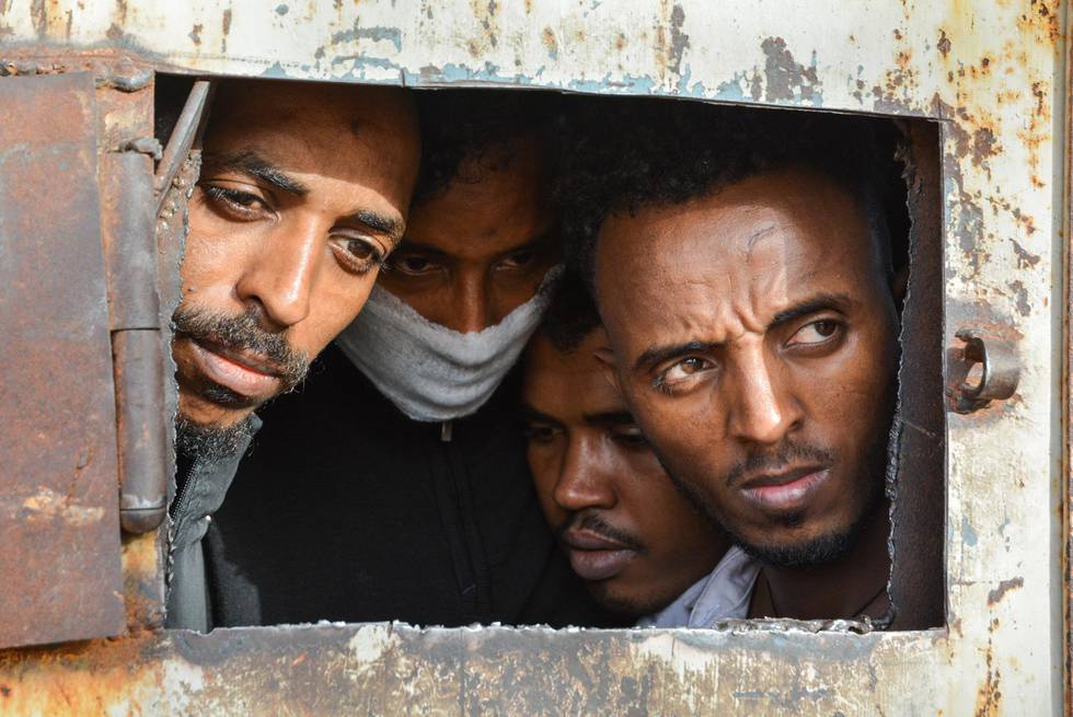 Refugees in Zintan DC at the gate of the main warehouse where 700 of them were detained. A tuberculosis outbreak has likely been raging for several months in the detention centre and some wear masks for fear of contamination. The main warehouse was emptied in June 2019, and the remaining people distributed among the other buildings within the detention centre compound.