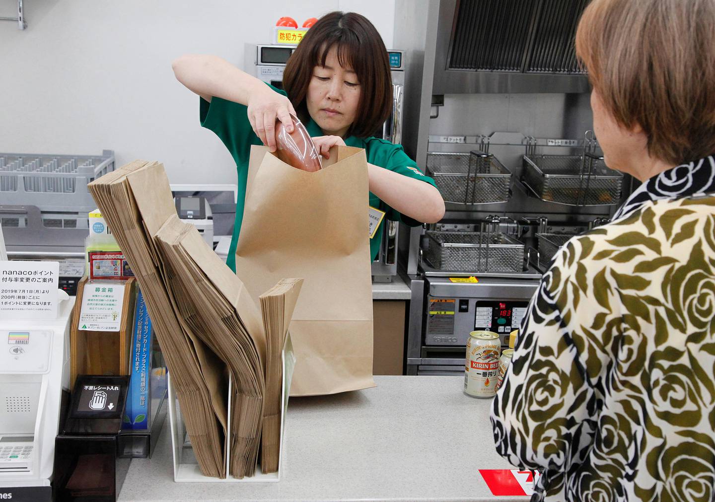 In this June 17, 2019, photo, a salesclerk puts goods into a paper bag after a customer purchased them, at a Seven-Eleven store in Yokohama, near Tokyo. Seven & i Holdings Co., a major Japanese convenience store operator, announced on May, 2019, a plan to replace all plastic shopping bags with paper by 2030 and all plastic packaging with paper, biodegradable or other reusable materials at its nearly 21,000 stores nationwide. Japan, as host of the Group of 20 Summit this weekend, hopes to lead the world in reducing plastic waste. (AP Photo/Koji Sasahara)