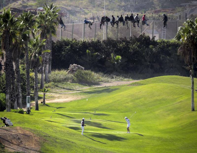 Afrikanske migranter prøver å komme seg over gjerdet fra Marokko til den spanske enklaven Melilla for å krysse Middelhavet til  Europa, mens golfspillerne fortsetter med sitt.