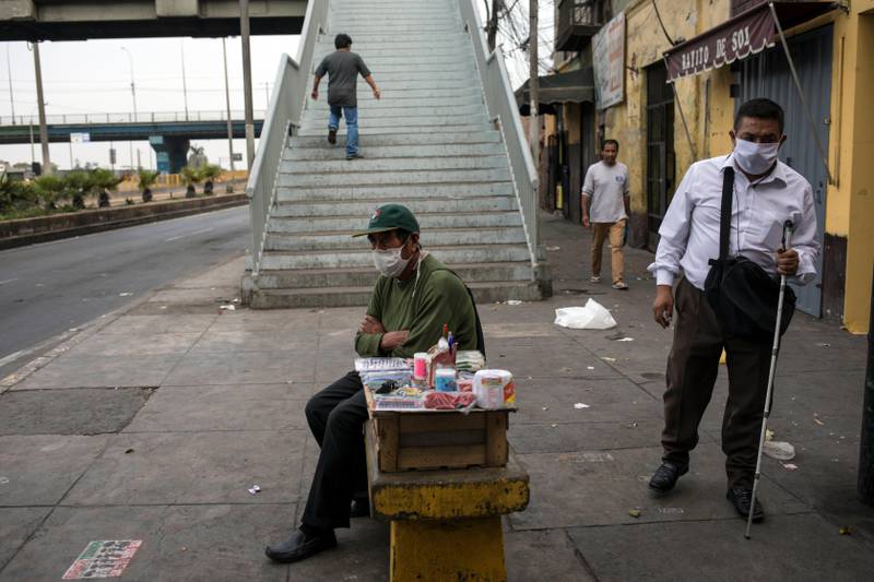 A street vendor using a protective face mask, waits for customers in a downtown largely absent of people, in Lima, Peru, Saturday, March 28, 2020, during the second week of a government decreed state of emergency that restricts residents to their homes to help contain the spread of the new coronavirus.  (AP Photo/Rodrigo Abd)