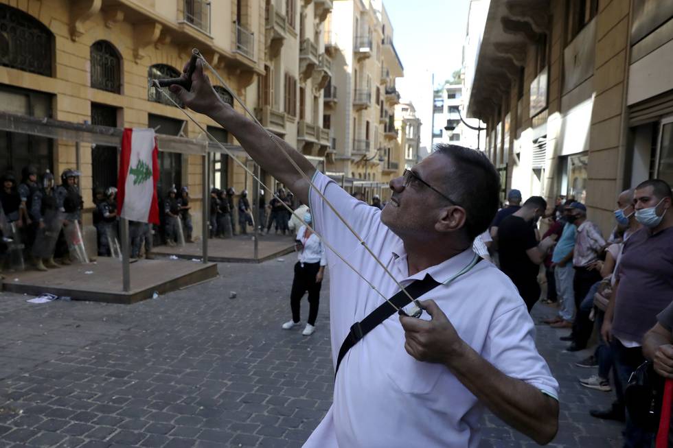 En mann skyter stein mot en bank i Beirut med sprettert. En folkemengde samlet seg onsdag utenfor banken for å kreve å få ut penger som er blitt blokkert på kontoene som følge av landets dype økonomiske krise. Lørdag kom meldingen om at strømforsyningen i landet kan bli borte i mange dager. Foto: Bilal Hussein / AP / NTB