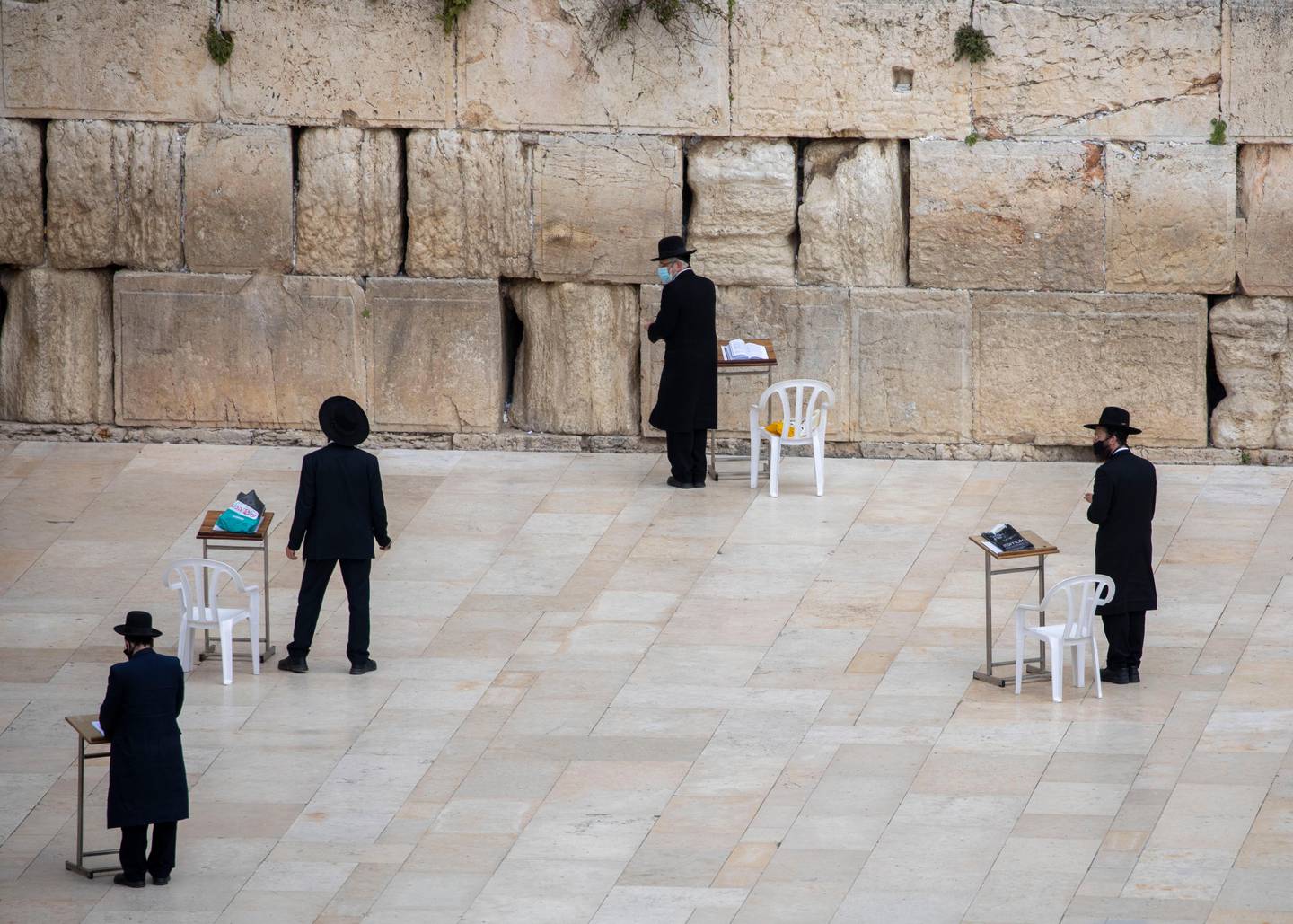 In this Tuesday, April 7, 2020 photo, ultra-Orthodox Jewish men wear face masks and keep social distancing, following the government's measures to help stop the spread of the coronavirus, pray at the Western Wall, the holiest site where Jews can pray in Jerusalem's Old City . As a modern pandemic afflicts the globe, Israeli Jews are being forced to scale back or cancel beloved traditions and rituals marking the start of Passover, the holiday celebrating Israelites' freedom from Egyptian bondage and referencing biblical plagues. Communal preparations have been canceled. Police are enforcing stay-at-home orders and a general lockdown on intercity travel through Friday morning. (AP Photo/Ariel Schalit)
