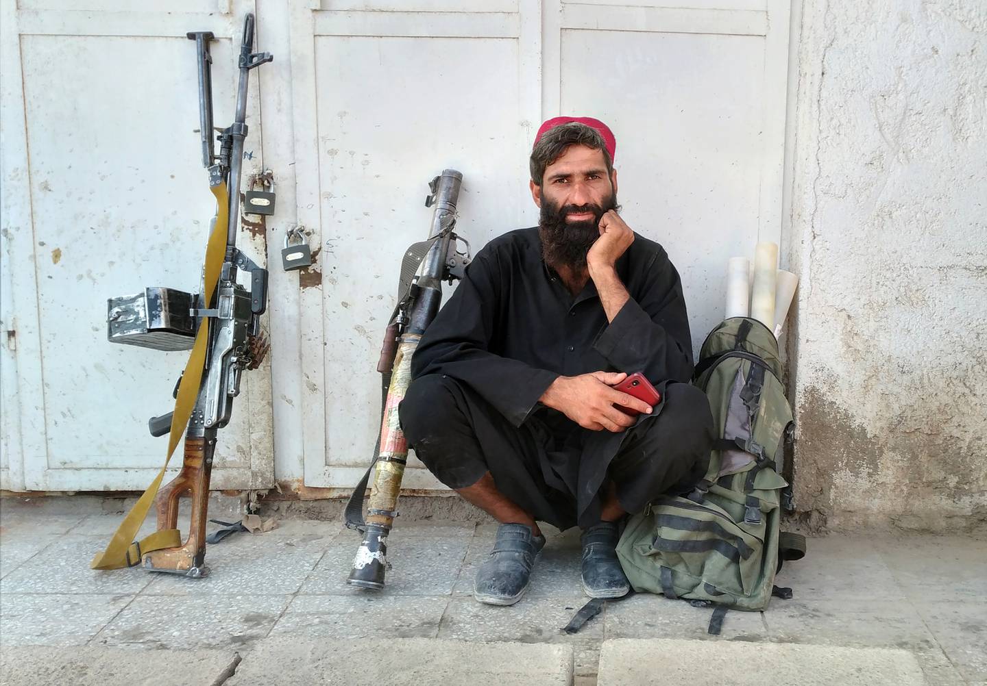 Bildet er av en Taliban-kriger som slapper av etter at opprørerne erobret provinshovedstaden Farah tidligere i uka. Foto: AP / NTB Han sitter ved siden av en sekk og våpen. Han er kledd i sort og har langt, mørkt skjegg. Han har på seg en rød lue.
