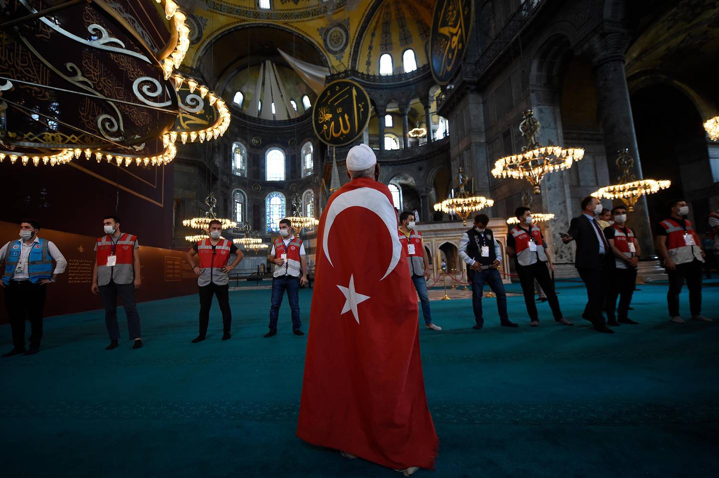 A man draped in a Turkish flag, stands as people walk inside the Byzantine-era Hagia Sophia following the inaugural Friday prayers, in the historic Sultanahmet district of Istanbul, Friday, July 24, 2020. Worshipers held the first Muslim prayers in 86 years inside the Istanbul landmark that served as one of Christendom's most significant cathedrals, a mosque and a museum before its conversion back into a Muslim place of worship. The conversion of the edifice, has led to an international outcry. (AP Photo/Yasin Akgul)