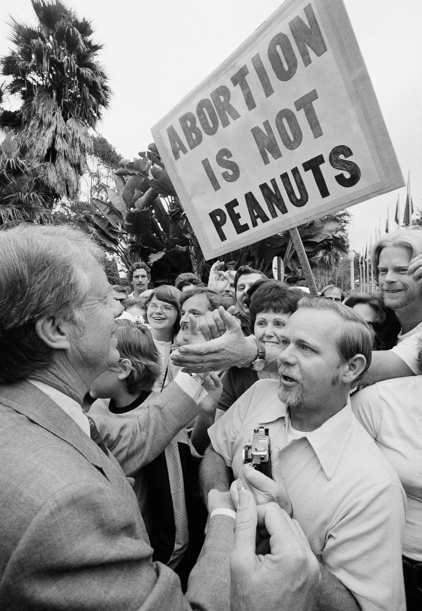 Jimmy Carter, on a brief campaign swing through Southern California, is stopped by a crowd outside the San Diego Zoo on Saturday, Sept. 25, 1976 before he made a short visit to zoo. Sign held up by someone in the crowd refers to one of the issues in the democratic platform. (AP Photo)