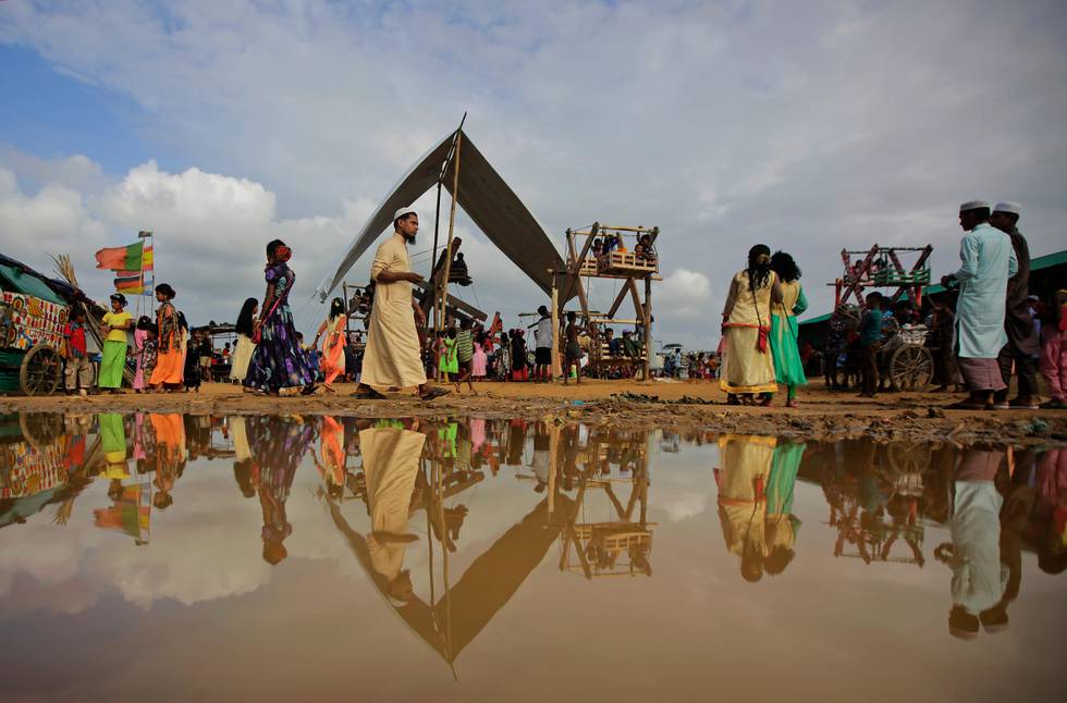 Rohingya refugees are reflected in a puddle during Eid al Adha celebration at Kutupalong refugee camp, Bangladesh, Wednesday, Aug. 22, 2018. Hundreds of thousands of Rohingya refugees in sprawling Bangladeshi camps are celebrating Eid al-Adha Wednesday amid festivity and confusion over whether they would ever be able to go back to Myanmar they fled amid violence and a massive crackdown. (AP Photo/Altaf Qadri)