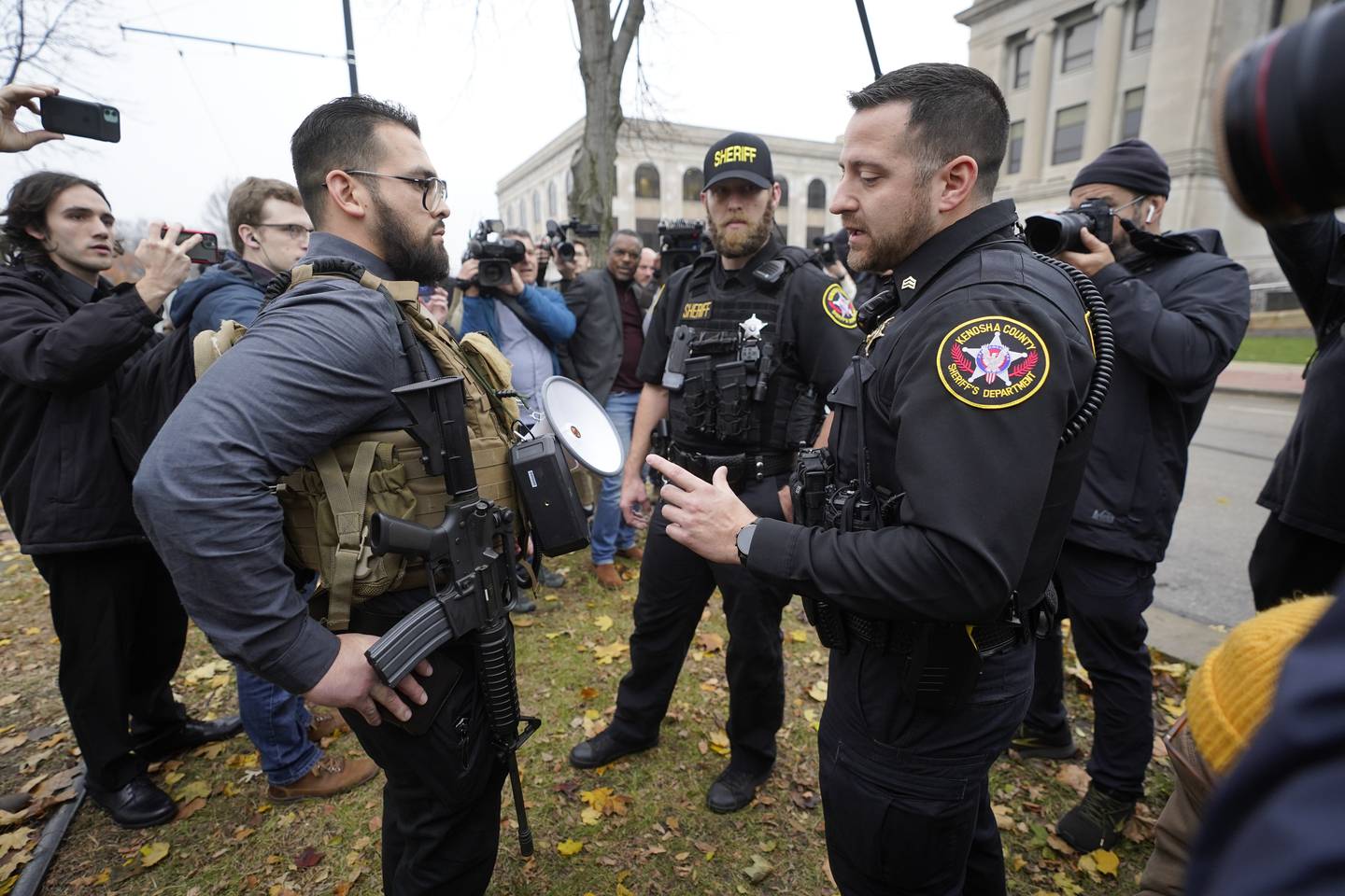 En politimann snakker med en demonstrant som bærer på en rifle utenfor tinghuset i Kenosha i Wisconsin mens rettssaken mot Kyle Rittenhouse pågikk i forrige uke. Det blir mer og mer akseptert å bære våpen på offentlig sted i USA. Foto: AP Photo / Paul Sancya / NTB