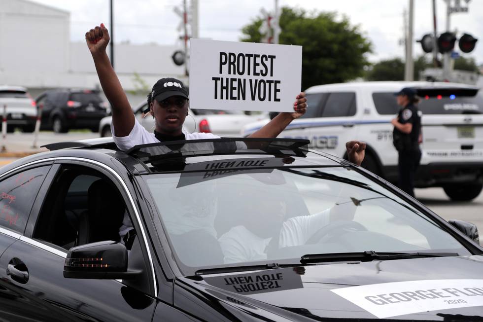A woman holds a sign reading "Protest then Vote" during a police escorted funeral procession  Wednesday, June 3, 2020, in Hallandale Beach, Fla., organized by the COOL Church to symbolize a day of mourning for those lives lost due to systemic racism. The protest is in conjunction with protests held throughout the country over the death of George Floyd, a black man who died after being restrained by Minneapolis police officers on May 25. (AP Photo/Lynne Sladky)