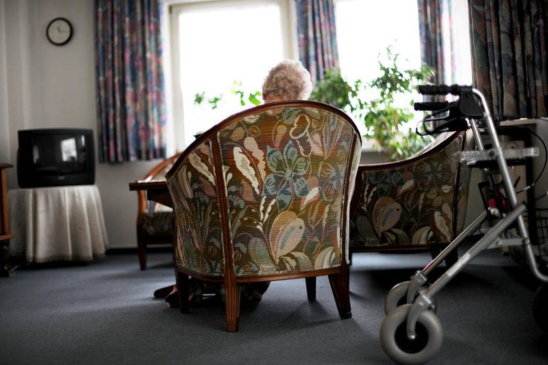 Illustrasjonsfoto. En gammel kvinne sitter på en stol og ser ut av vinduet.