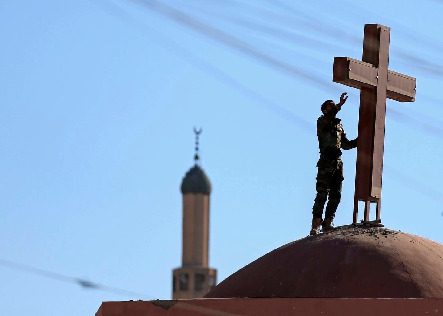 An Iraqi Kurdish Muslim Peshmerga fighter sets a cross on top of a church, which was damaged by Islamic State fighters during their occupation of Bashiqa, east of Mosul, Iraq, Wednesday, Dec. 7, 2016. A senior Iraqi commander said Wednesday that special forces captured a new neighborhood from Islamic State militants in eastern Mosul, the latest gain in a massive government military operation now in its seventh week. (AP Photo/Hadi Mizban)