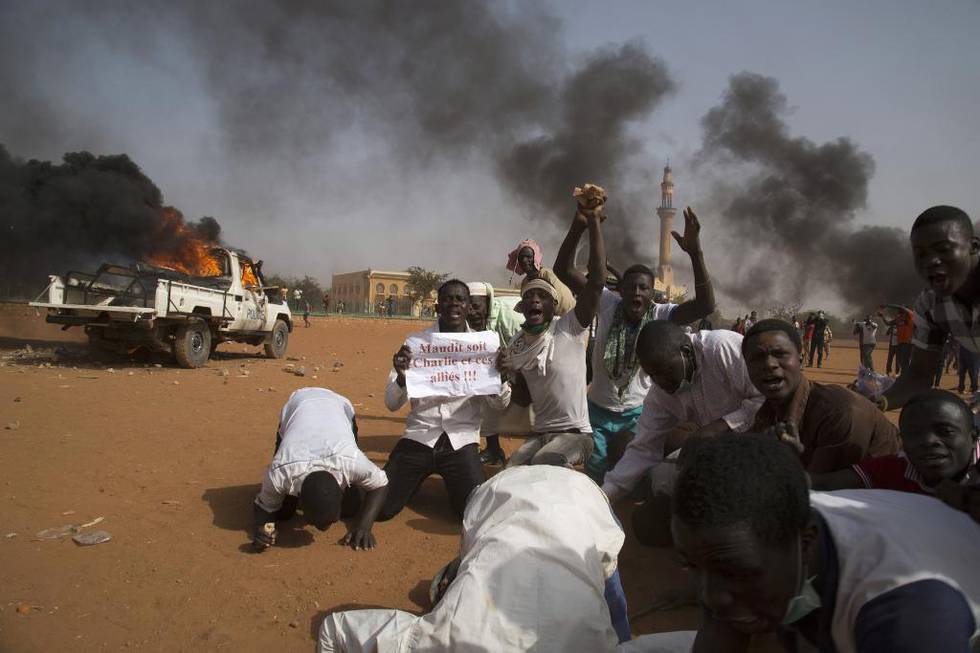 Mens en politibil brenner foran den store moskeen i Niamey holder demonstranter opp en plakat med teksten «Charlie og hans allierte er forbannet». 75 kirker og bygninger ble brent i Niger i helgen.