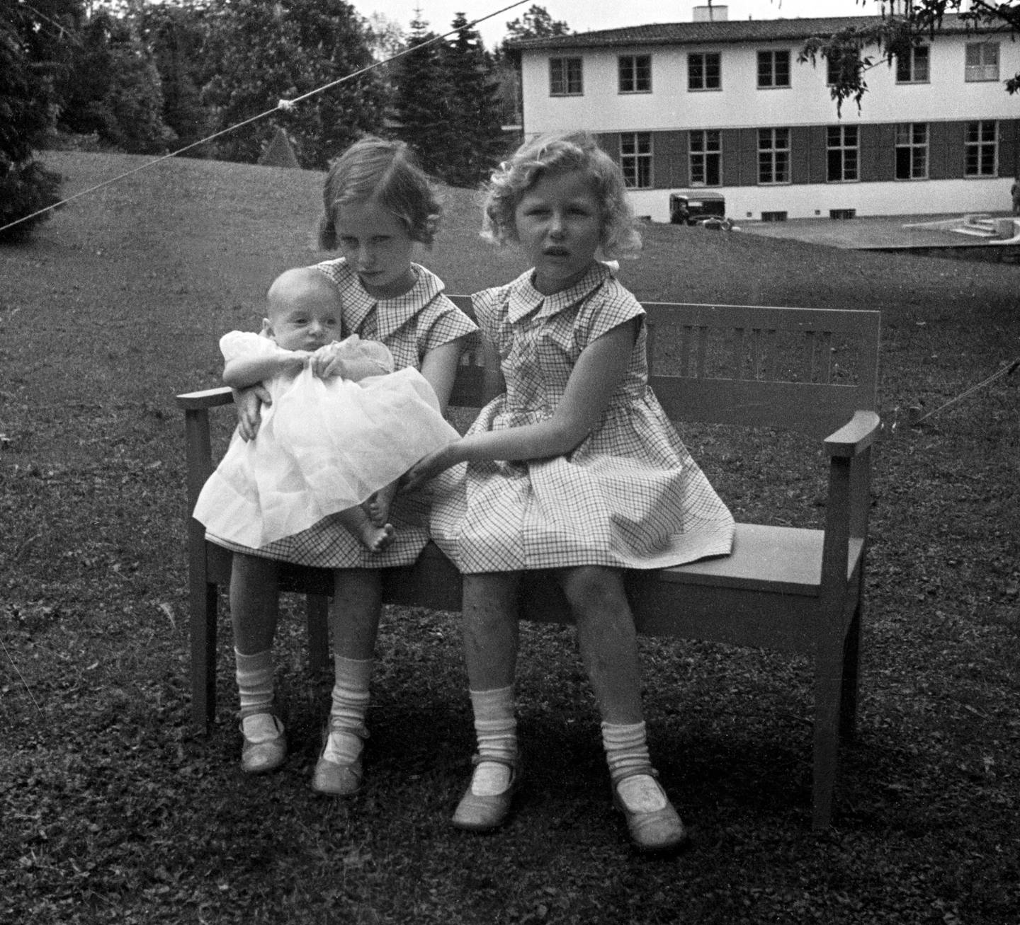 SKAUGUM Juni 1937.  Prinsesse Ragnhild  (tv) og prinsesse Astrid med prins Harald, ca seks måneder gammel. De tre sammen, sittende på en benk i hagen.
Foto: NTB scanpix