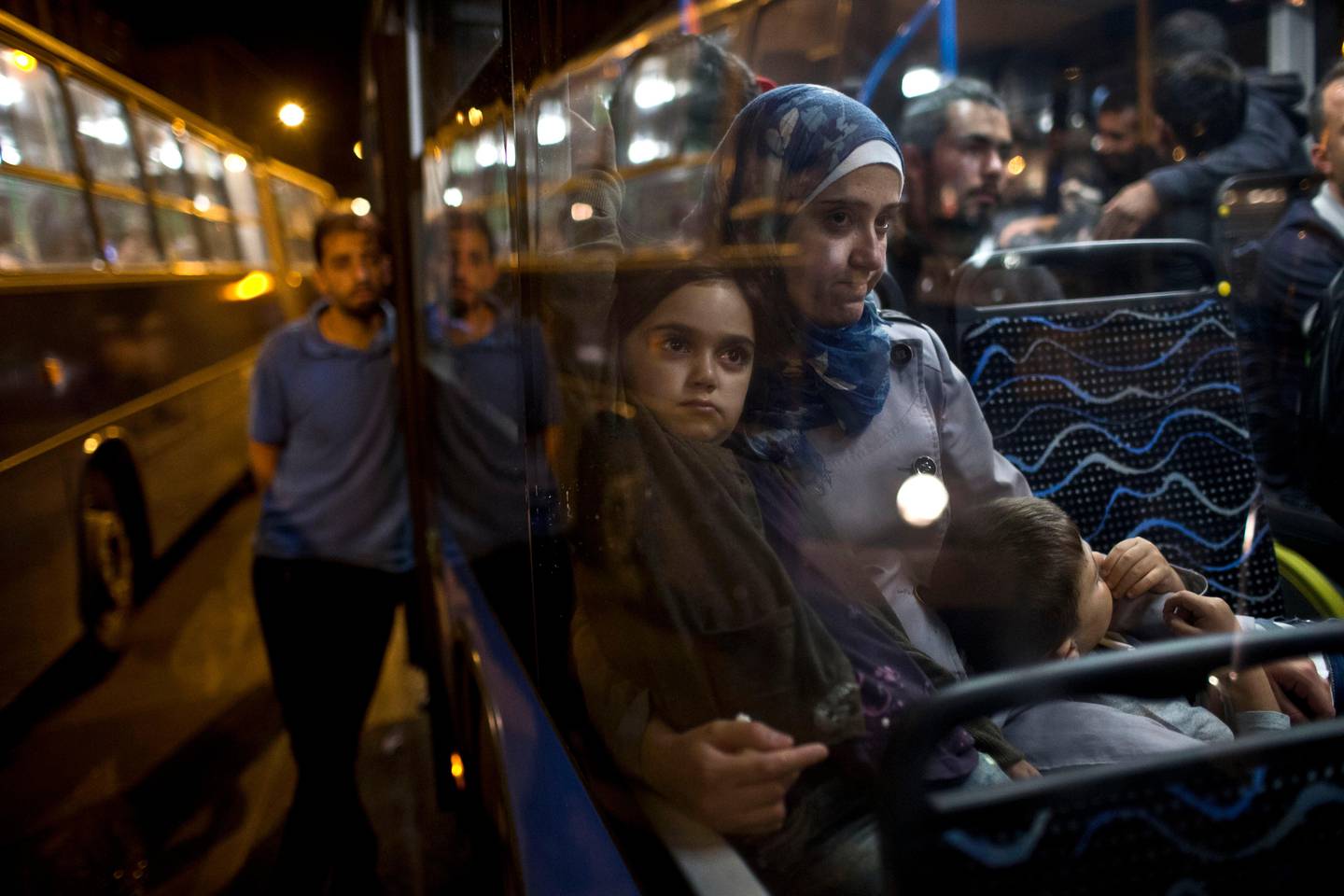 A woman and her children sit as they have boarded a bus provided by Hungarian authorities for migrants and refugees at Keleti train station in Budapest, Hungary, Saturday, Sept. 5, 2015. Hundreds of migrants boarded buses provided by Hungary's government as Austria in the early-morning hours said it and Germany would let them in. Austrian Chancellor Werner Faymann announced the decision early Saturday after speaking with Angela Merkel, his German counterpart - not long after Hungary's surprise nighttime move to provide buses for the weary travelers from Syria, Iraq and Afghanistan.  (AP Photo/Marko Drobnjakovic)