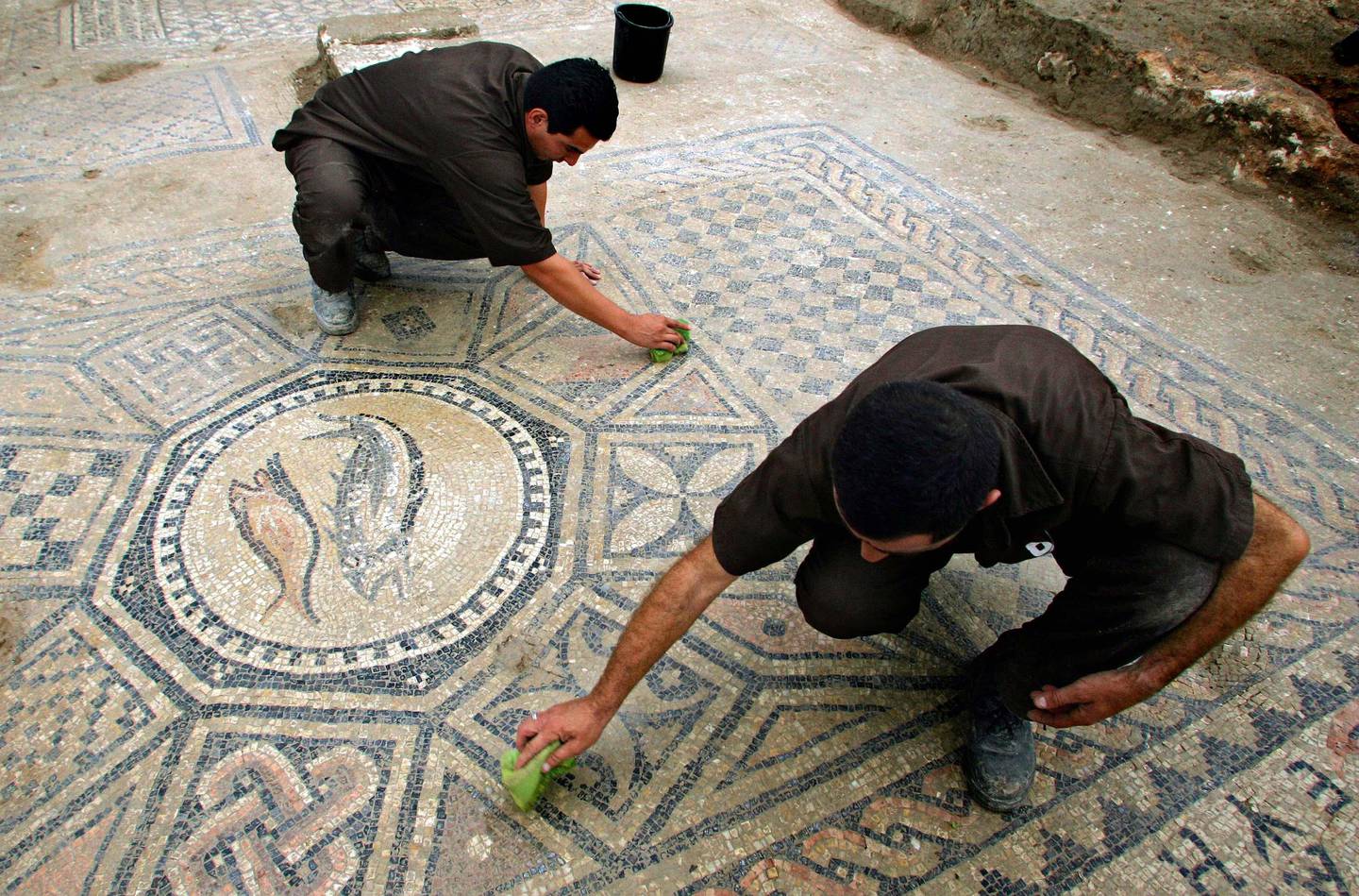 ** CAPTION CORRECTION, CORRECTS NAME OF PRISONER TO RAMIL RAZILO, NOT RIZLOV RAMIL AND MEIMON BITON, NOT BITON MAYMON ** Israeli prisoners Ramil Razilo, top, and Meimon Biton, bottom, clean a section of a Christian mosaic floor dating to the third or fourth century A.D., in the compound of the Megiddo prison in northern Israel , Sunday  Nov. 6, 2005. Israeli archaeologists on Saturday said they have discovered what may be the oldest Christian church in the Holy Land on the grounds of a prison near the biblical site of Armageddon. The Israeli Antiquities Authority said the ruins are believed to date back to the third or fourth centuries, and include references to Jesus and images of fish, an ancient Christian symbol. (AP Photo/Ariel Schalit)