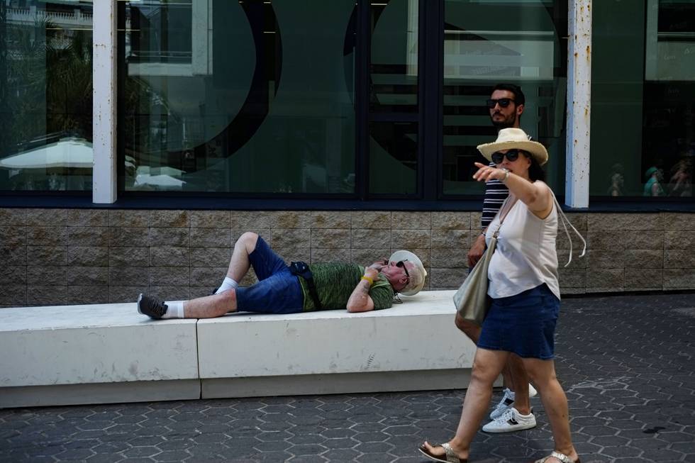 A tourist rests while people walk during a sunny spring day, in Benidorm, south-east Spain, Saturday, May 21, 2022. A mass of hot, dry air carrying dust from North frica has pushed temperatures up to 15 degrees above average with the mercury topping 40 C (104 F) in parts of the country. (AP Photo/Alvaro Barrientos)