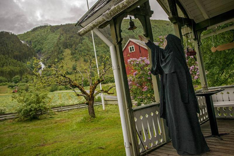 TIDLEG OPPE: Nonnen Arhontia ringer i bjølla utanfor hovudhuset på prestegarden, for å kalle inn til morgonbøn. Oppe i fjellsida kjem Dyrdalsfossen buldrande. 