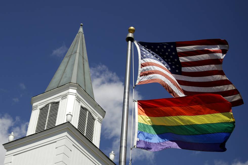 FILE - A gay pride rainbow flag flies along with the U.S. flag in front of the Asbury United Methodist Church in Prairie Village, Kan, on April 19, 2019.  A group of theologically conservative United Methodists plans to launch a new worldwide denomination on May 1, 2022.  This will begin the breakup of the third-largest religious body in the U.S.  (AP Photo/Charlie Riedel, File)