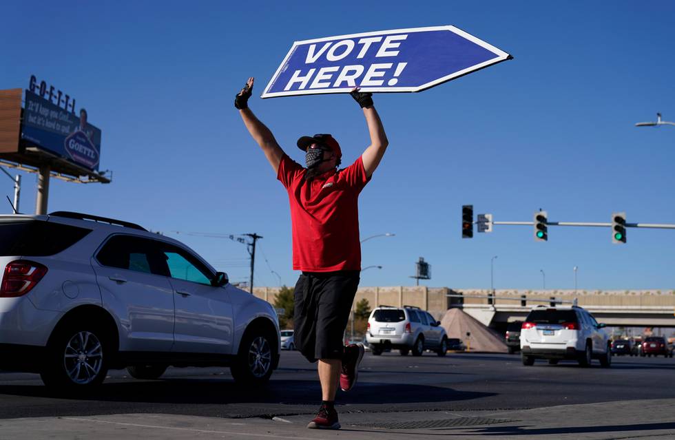 Sign-spinner Thomas Salazar holds a sign that reads "Vote Here!" outside a polling place on the final day of early voting Friday, Oct. 30, 2020, in Las Vegas. (AP Photo/John Locher)