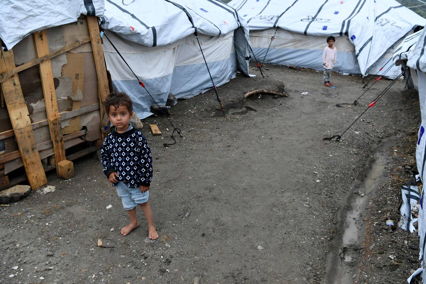 A migrant boy stands barefoot between tents after a rainstorm outside the Moria refugee camp on the northeastern Aegean island of Lesbos, Greece, Wednesday, Sept. 25, 2019. Authorities on the Greek island of Lesbos have partly reopened the country's largest refugee camp to newly arrived migrants despite acute overcrowding. (AP Photo/Michael Varaklas)
