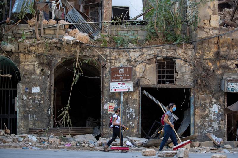 Women with brooms pass by a historic building damaged by Tuesday's explosion in the Gemmayzeh neighborhood,  Beirut, Lebanon, Saturday, Aug. 8, 2020. Senior officials from the Middle East and Europe started arriving in Lebanon Saturday in a show of solidarity with the tiny country that suffered a deadly blast this week which caused large-scale damage to the capital Beirut. (AP Photo/Hassan Ammar)