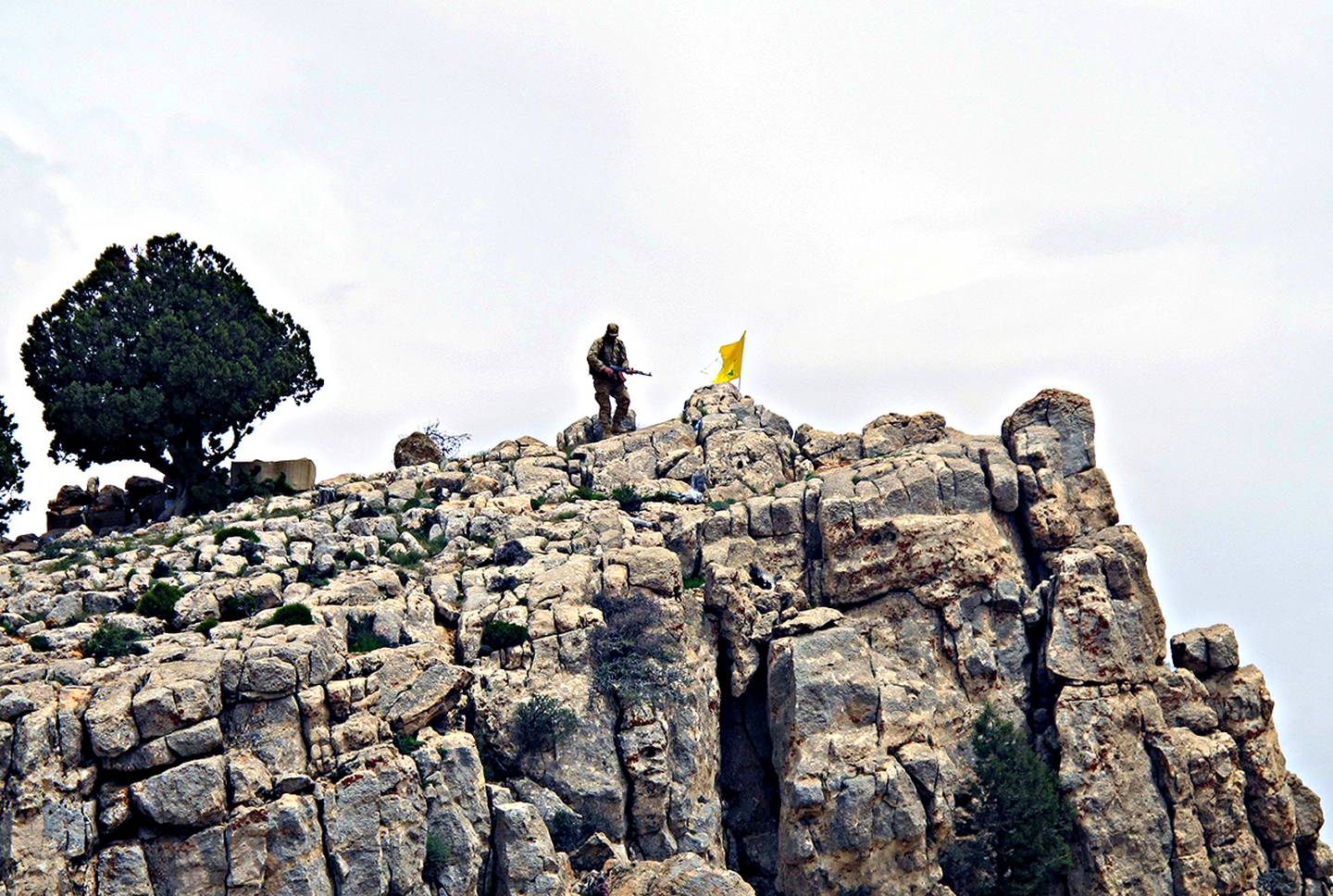 En kriger fra Hizbollah står ved siden av gruppens gule flagg på et fjell i regionen Qalamoun i Syria.