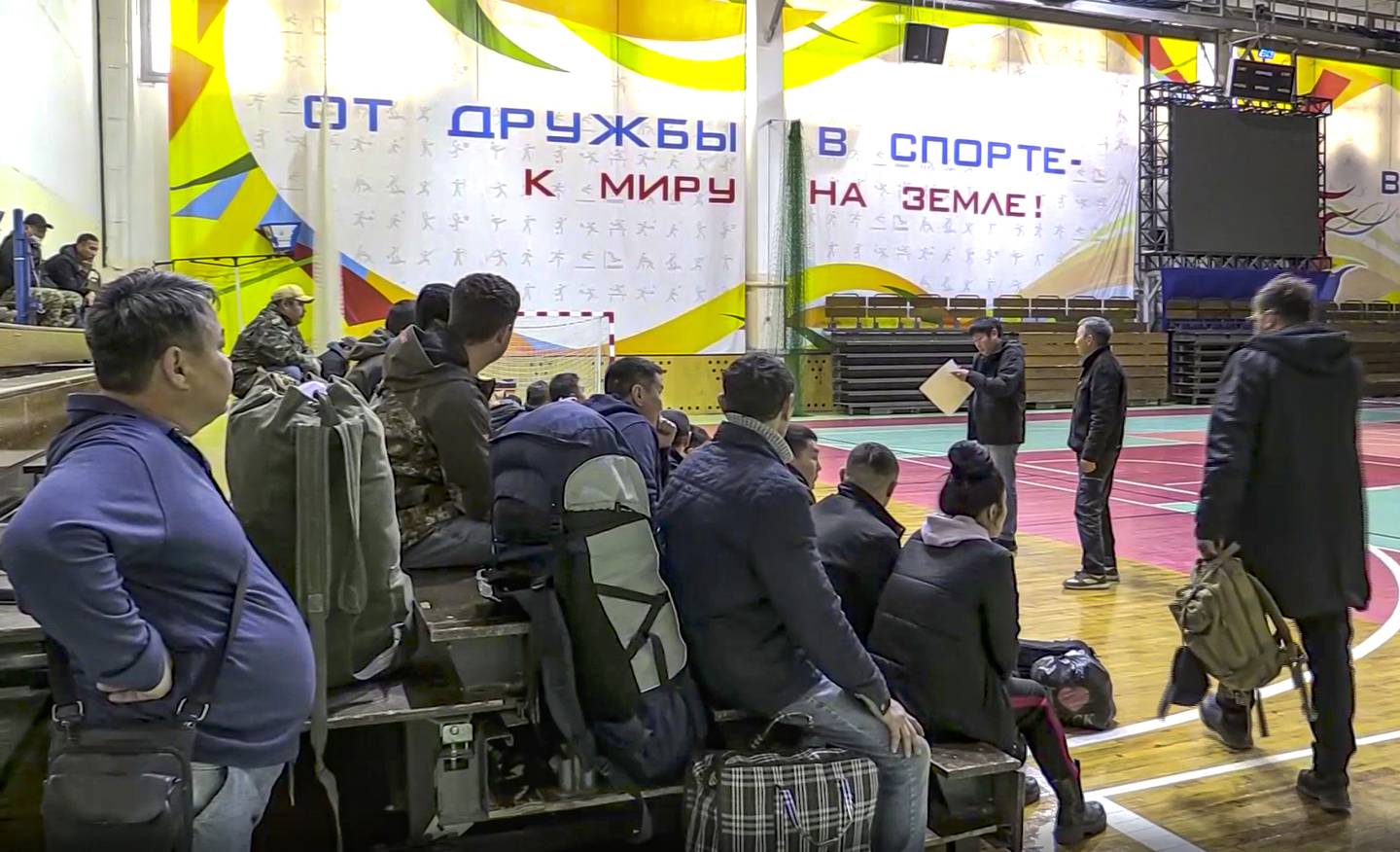 In this image taken from video, Russian draftees gather inside an indoor stadium turned into collection center for the draftees, who will be sent to the military units of the Eastern Military District, in Yakutsk, Russia, Friday, Sept. 23, 2022. Mobilization is underway in Russia's Far Eastern region of Yakutia after President Vladimir Putin ordered a partial mobilization of reservists Wednesday to bolster his forces in Ukraine. The words in the background read "From friendship in sports to peace on earth!". (AP Photo)