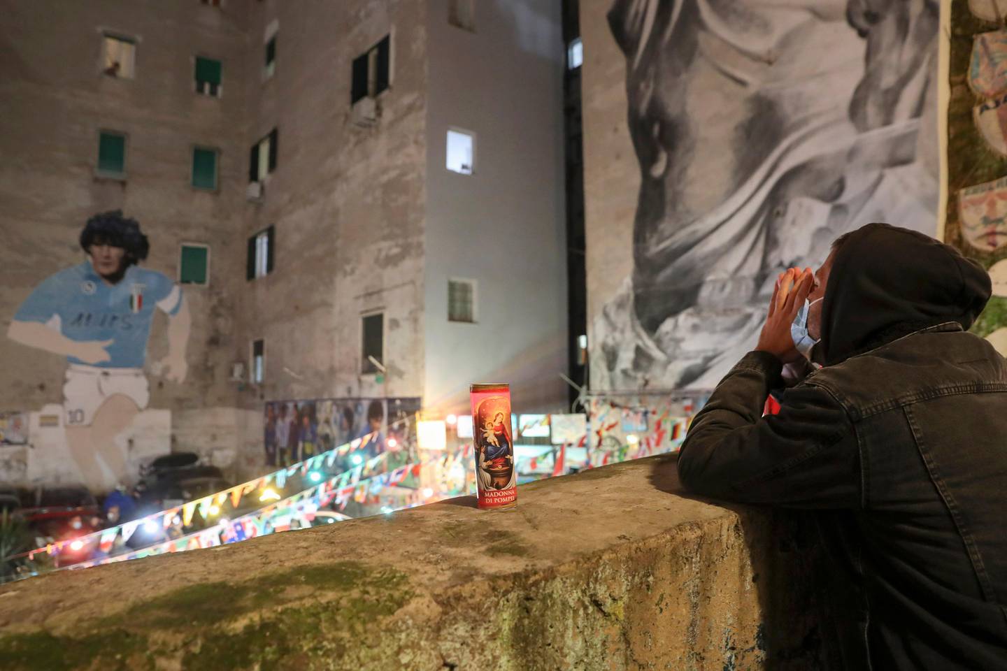 A man prays under a mural depicting soccer legend Diego Maradona, in Naples, Italy, Wednesday, Nov. 25, 2020. Diego Maradona has died. The Argentine soccer great was among the best players ever and who led his country to the 1986 World Cup title before later struggling with cocaine use and obesity. He was 60. (AP Photo/Salvatore Laporta)