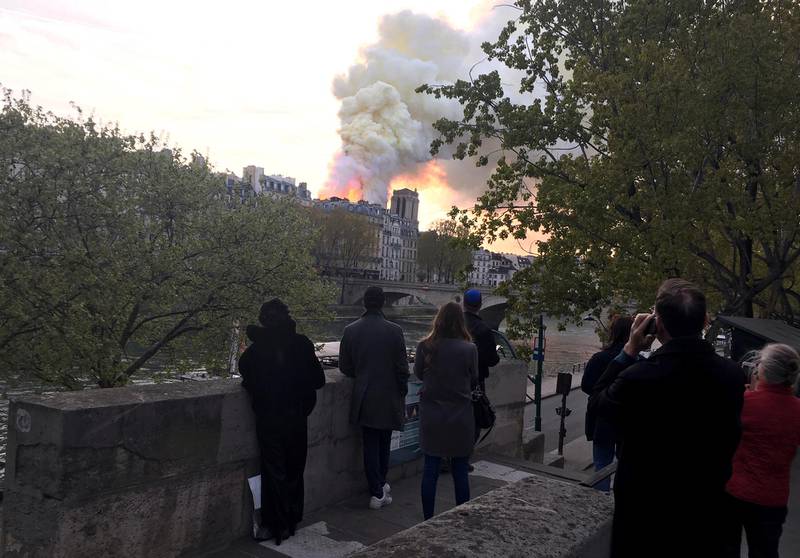 People watch Notre Dame cathedral burning in Paris, Monday, April 15, 2019. Massive plumes of yellow brown smoke is filling the air above Notre Dame Cathedral and ash is falling on tourists and others around the island that marks the center of Paris. (AP Photo/Oleg Cetinic)