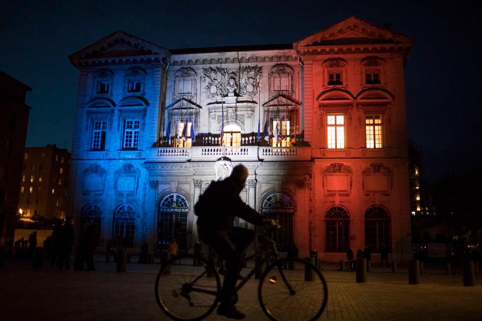 A cyclist passes Marseille's town hall lit up in the French Tricolor to honor slain teacher Samuel Paty, Wednesday, Oct. 21, 2020. French history teacher Samuel Paty was beheaded in Conflans-Sainte-Honorine, northwest of Paris, by a 18-year-old Moscow-born Chechen refugee, who was later shot dead by police. (AP Photo/Daniel Cole)
