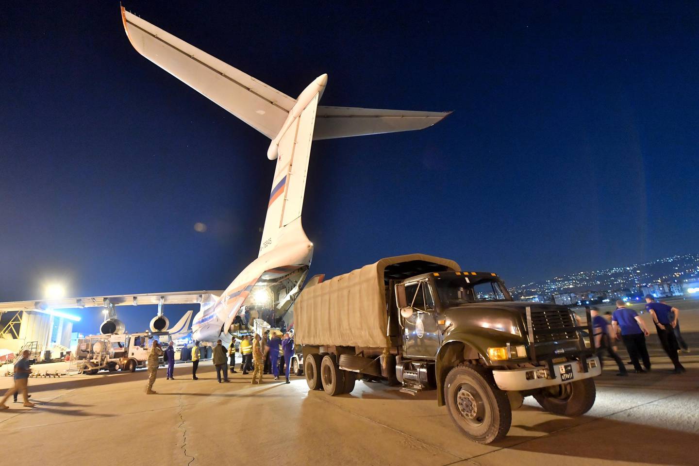 In this photo provided by Russian Emergency Situations Ministry press service, workers unload boxes of Russian aid supplies from a Russian cargo plane into a truck at an airport in Beirut, Lebanon, late Wednesday, Aug. 5, 2020. Russia's emergency officials say the country sent five planeloads of aid to Beirut after an explosion in the Lebanese capital's port killed at least 100 people and injured thousands on Tuesday. Russia's Ministry for Emergency Situations sent rescuers, medical workers, a makeshift hospital and a lab for coronavirus testing to Lebanon. (AP Photo/Ministry of Emergency Situations press service via AP)