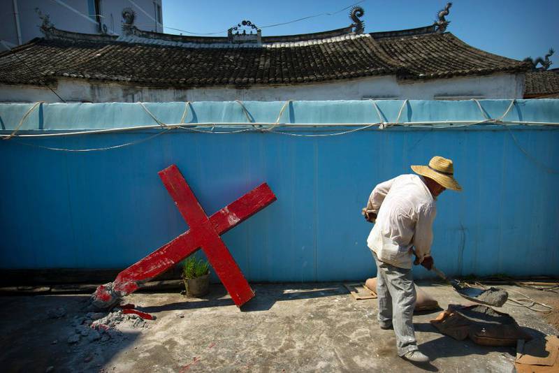 En kineser blander sement for å sette opp igjen korset på den protestantiske kirken i landsbyen Taitou. Bildet er fra juli i fjor. Myndighetene i provinsen Zhejiang har revet ned mange kors på kirker og bygninger.