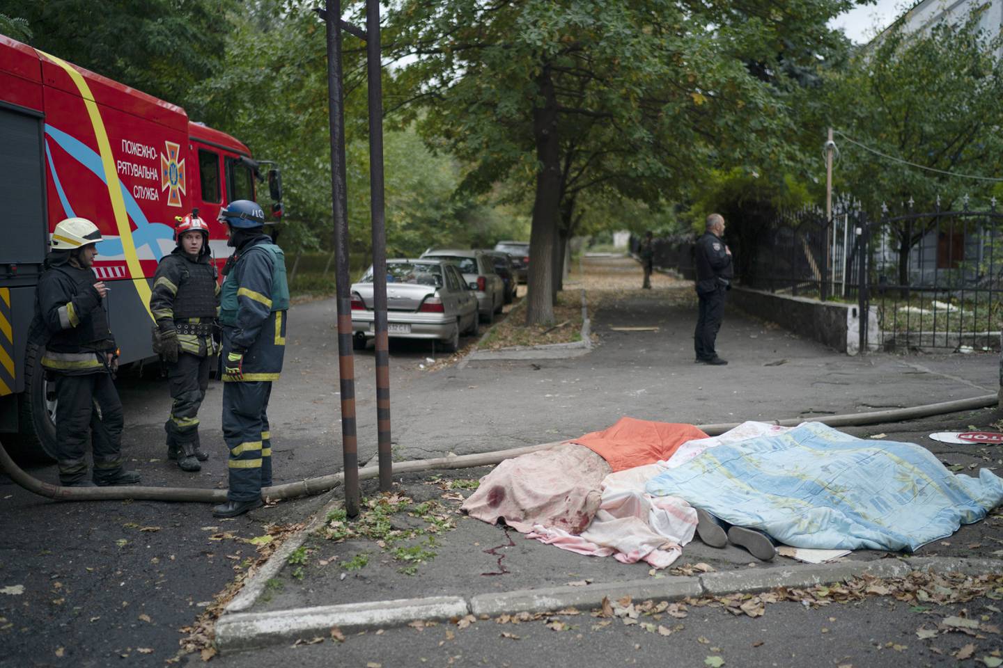 Firefighters stand next to three bodies, covered by blankets, following a Russian attack in Dnipro, Ukraine, Monday, Oct. 10, 2022. Explosions on Monday rocked multiple cities across Ukraine, including missile strikes on the capital Kyiv for the first time in months. (AP Photo/Leo Correa)