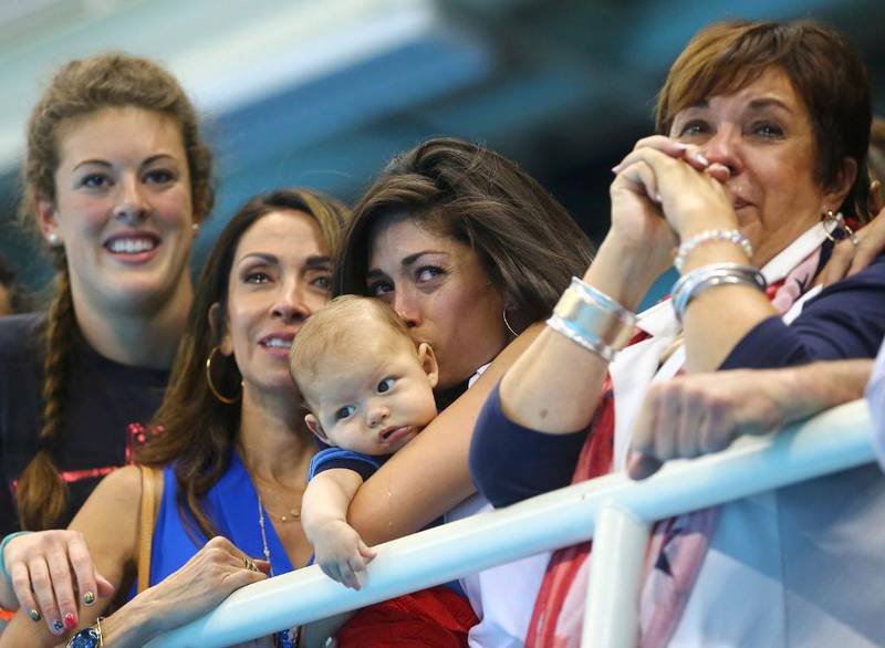 Nicole Johnson, Michael Phelps forlovede, kysser parets sønn Boomer mens hun følger med på kjæresten som tar nok en gullmedalje i svømmebassenget. Til høyre er moren til Phelps, Deborah Phelps.